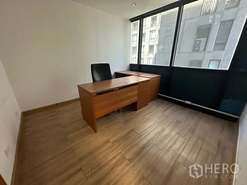 Office Space for rent or sale - Compact private office with wooden desk and tall windows facing neighboring building.
