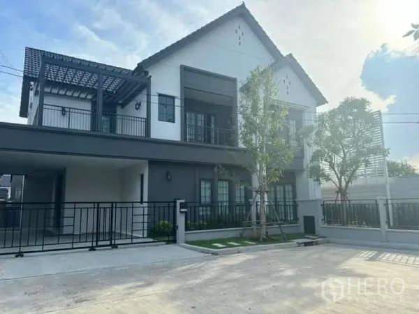 Detached House for rent in Bang Phli, Samut Prakan - Front exterior of detached house with gated carport, balcony and trees.