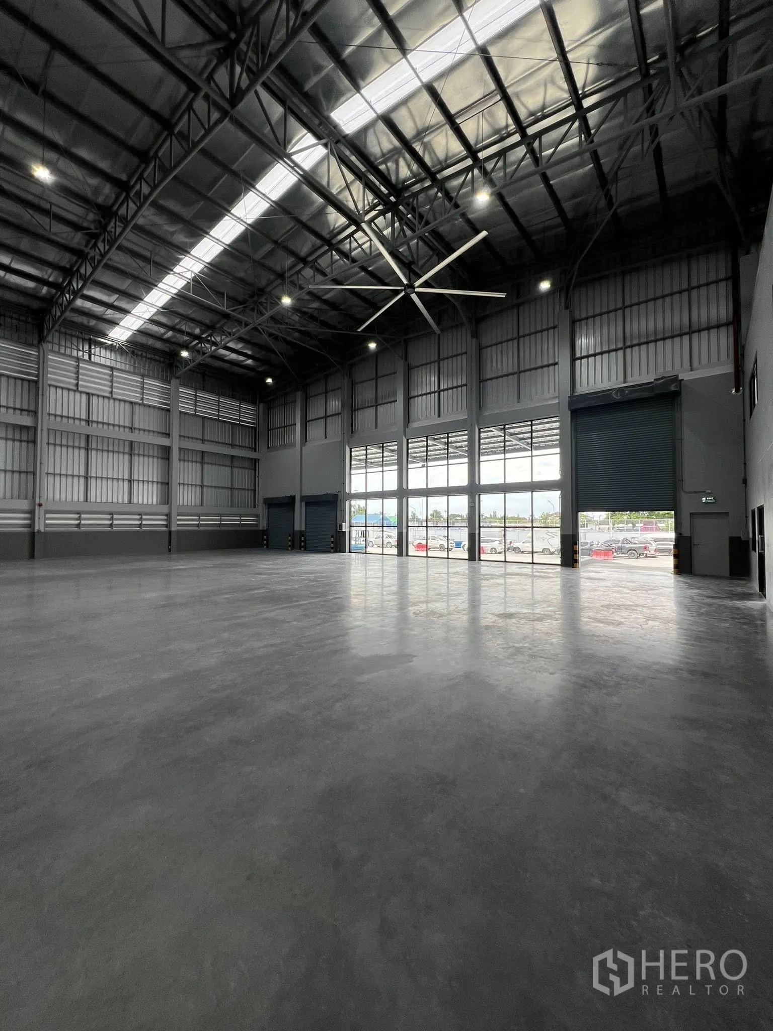 Warehouse for rent in Phra Pradaeng, Samut Prakan - Front bay of the warehouse with roller shutter doors, glazed facade, and a big ceiling fan.
