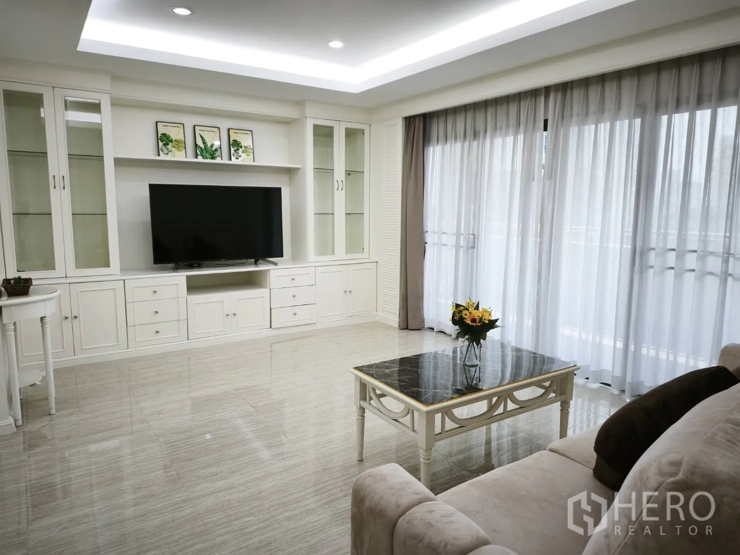 Condominium for rent in Watthana, Bangkok - Living area with a marble-top coffee table, large TV console, and full-height windows with curtains.