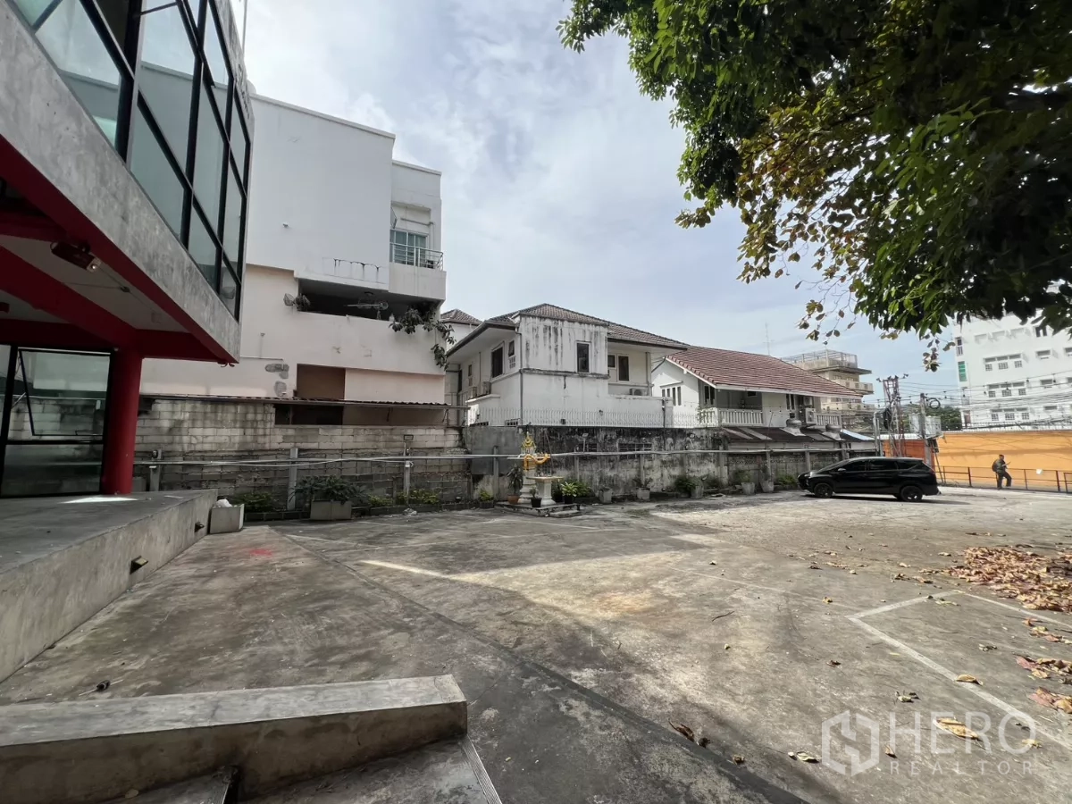 独立商业地产 出租在Din Daeng, Bangkok - 树荫下的大型前场停车区，邻近玻璃立面建筑。