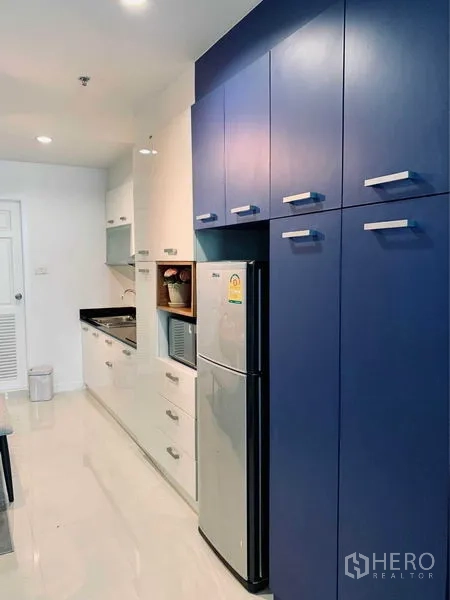 คอนโด ให้เช่าในWatthana, Bangkok - ตู้ครัวสูงสีน้ำเงินข้างตู้เย็นสแตนเลสและช่องเก็บของ