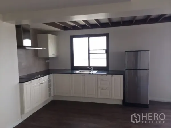 Condominium for rent or sale in Chatuchak, Bangkok - Bright L-shaped kitchen with white cabinets, dark countertops, window, and stainless-steel refrigerator.