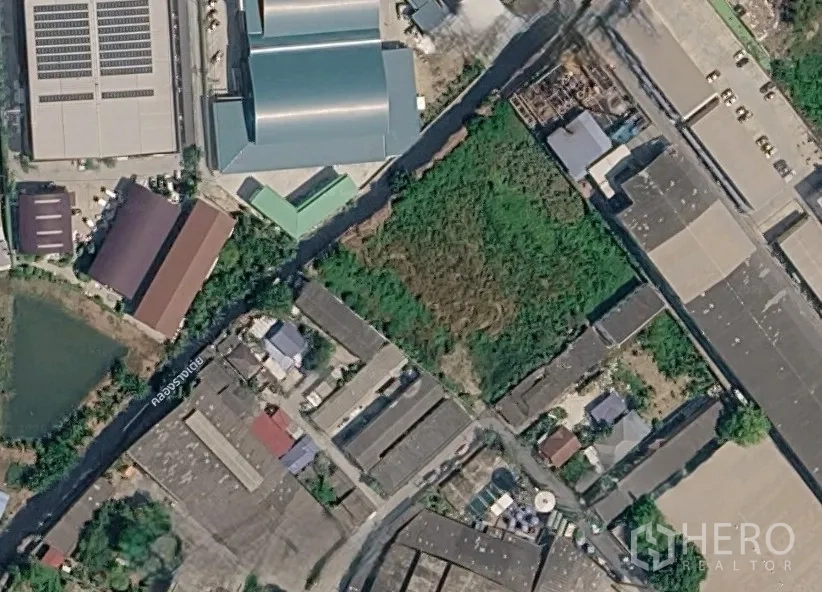 Land for sale in Sam Phran, Nakhon Pathom - Satellite view of a vacant green plot surrounded by warehouses and access roads in an industrial area.