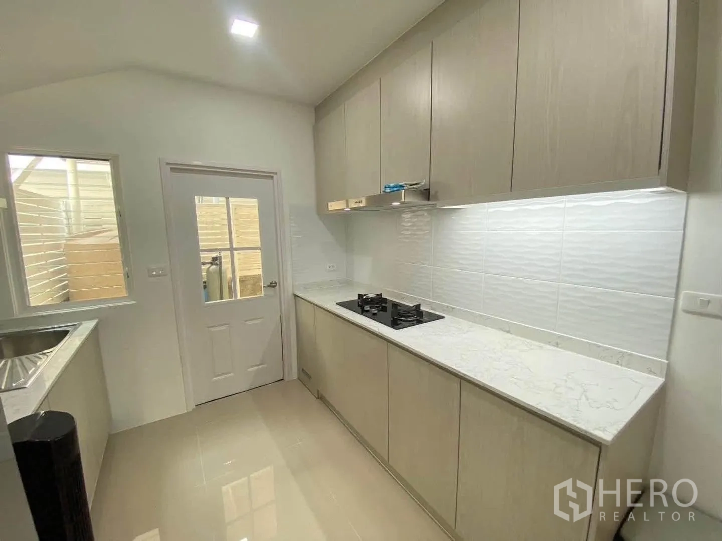 Detached House for rent in Mueang Samut Prakan, Samut Prakan - Modern closed kitchen with gas hob, white backsplash, and door to yard.