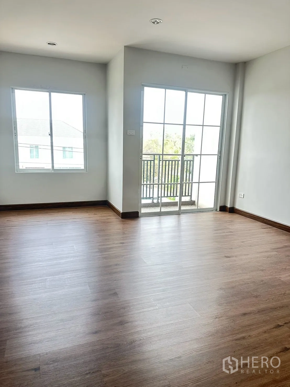 Home Office for rent in Khlong Luang, Pathum Thani - Upper-floor room with wood-look flooring, two windows and a sliding glass door to a small balcony.
