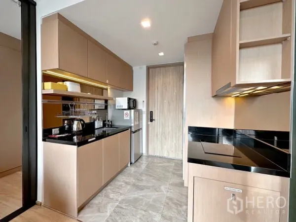 Condominium for sale in Watthana, Bangkok - Compact built‑in kitchen with black stone countertop, upper cabinets, and microwave, fridge and cooktop.