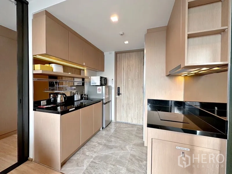 Condominium for sale in Watthana, Bangkok - Compact built‑in kitchen with black stone countertop, upper cabinets, and microwave, fridge and cooktop.