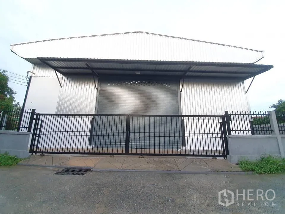 货栈 出租在Bang Khen, Bangkok - 仓库正面图，卷闸门关闭，临街黑色滑动围栏门。