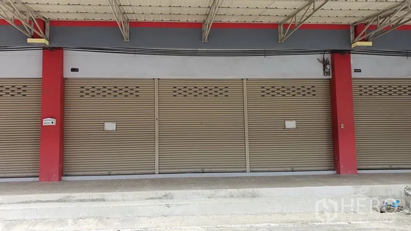 Shophouse for rent in Thon Buri, Bangkok - Close-up of the ground-floor shopfront with beige roller shutters and a covered walkway.