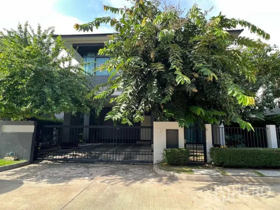 บ้าน ให้เช่าหรือขายในBang Kapi, Bangkok - ด้านหน้าบ้านสองชั้นสไตล์โมเดิร์น พร้อมรั้วและทางรถเข้าท่ามกลางต้นไม้ร่มรื่น