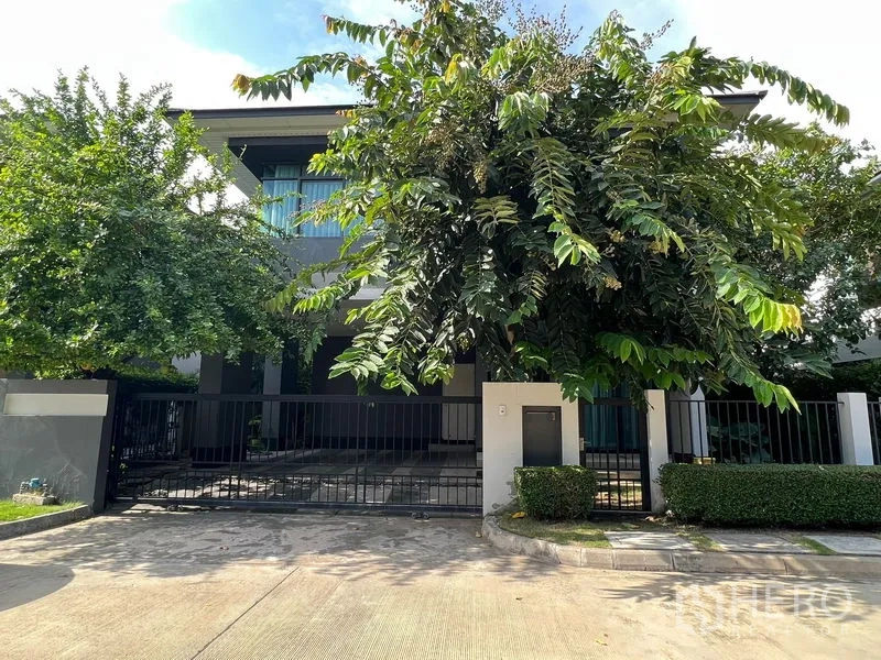 บ้าน ให้เช่าหรือขายในBang Kapi, Bangkok - ด้านหน้าบ้านสองชั้นสไตล์โมเดิร์น พร้อมรั้วและทางรถเข้าท่ามกลางต้นไม้ร่มรื่น