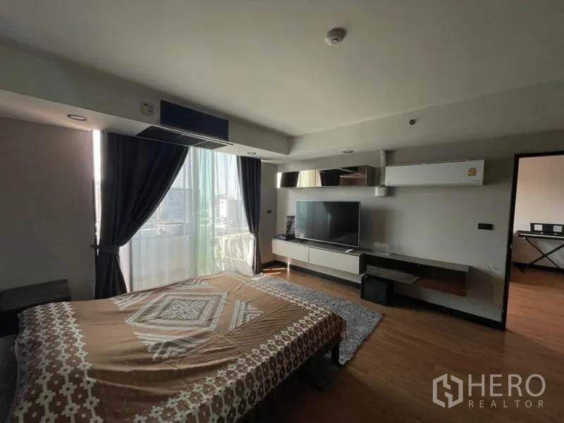 Condominium for sale in Chatuchak, Bangkok - Spacious bedroom with large window, TV wall unit and access to a private balcony.