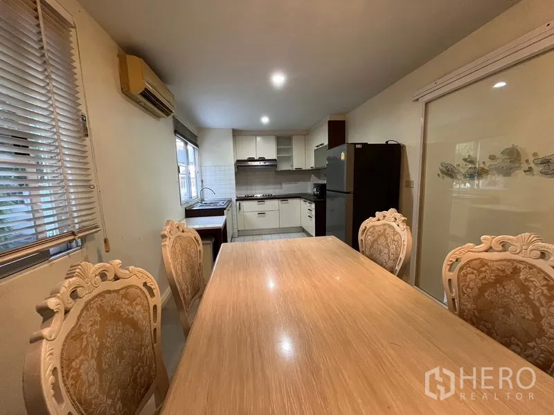 Townhouse for rent in Phaya Thai, Bangkok - Open dining and kitchen zone with wooden table, ornate chairs, fridge and sliding glass door.