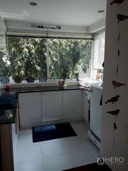 Condominium for rent in Pathum Wan, Bangkok - White U-shaped kitchen with expansive windows, leafy bamboo views, and ample countertop space.
