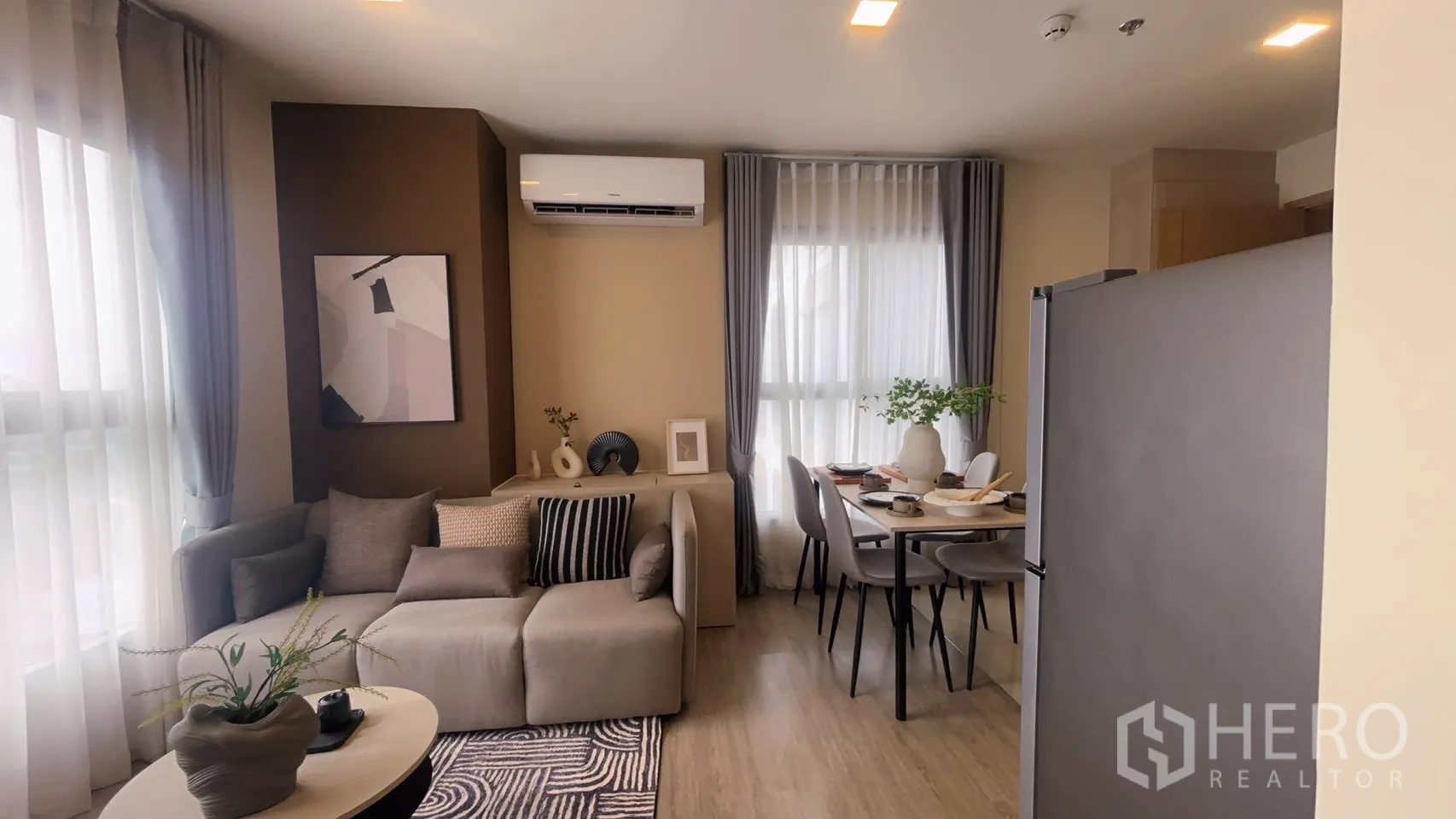 Condominium for rent in Watthana, Bangkok - View across the living space showing sofa, wall art, air conditioner, and dining set near windows.