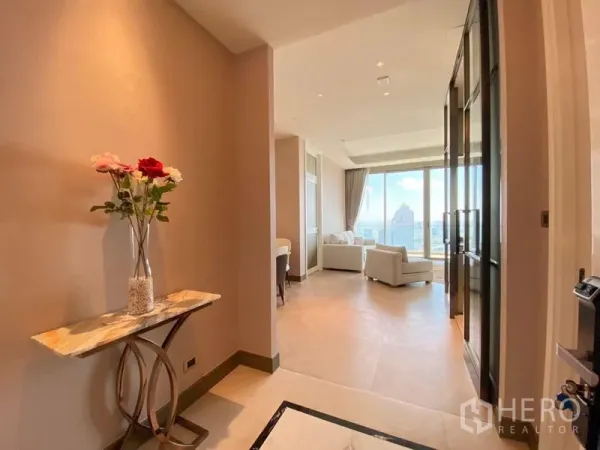 Condominium for rent in Khlong San, Bangkok - Bright entry hall with a marble console and flowers leading to a living room with floor‑to‑ceiling windows and city view.