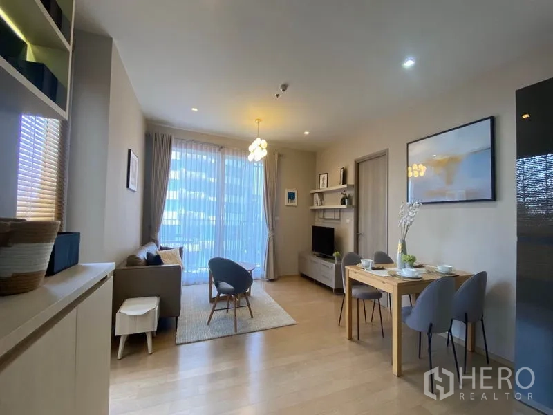 Condominium for rent or sale in Khlong Toei, Bangkok - Cozy living room with sofa, dining table and full-height curtains facing a balcony.