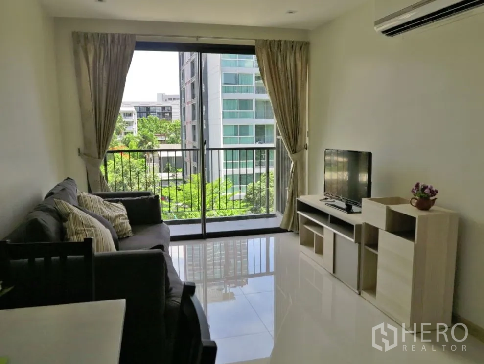 คอนโด ให้เช่าหรือขายในWatthana, Bangkok - ห้องนั่งเล่นสว่างพร้อมโซฟา ตู้วางทีวี และประตูกระจกออกสู่ระเบียง มองเห็นต้นไม้ ใกล้ BTS เอกมัย