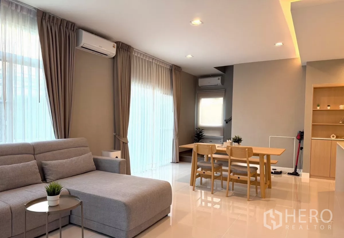 Detached House for rent in Prawet, Bangkok - Bright living room with grey sectional sofa, dining set and full-length curtains