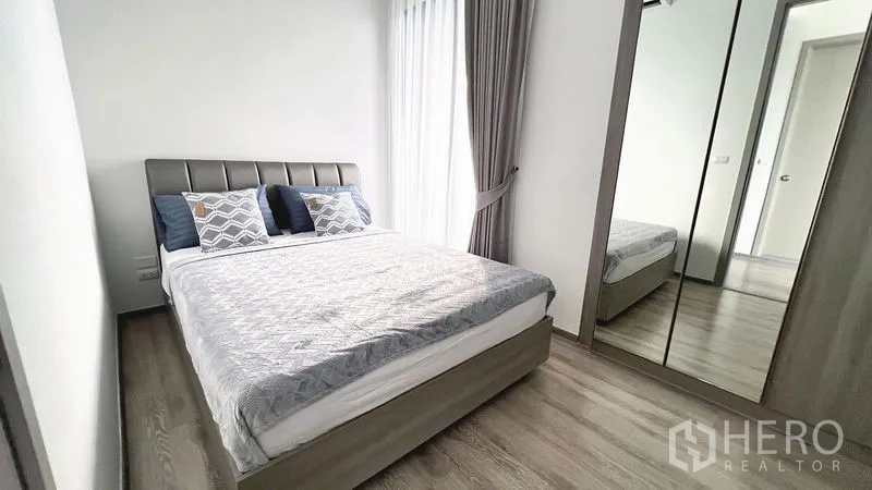 Condominium for rent in Watthana, Bangkok - Second bedroom with queen bed, mirrored wardrobe, wood flooring, and tall window with curtains.