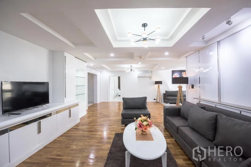 คอนโด ให้เช่าในKhlong Toei, Bangkok - มุมห้องนั่งเล่นพร้อมชั้นวางทีวี โซฟาสีเทา และฝ้าแบบหลุมพร้อมไฟดาวน์ไลท์