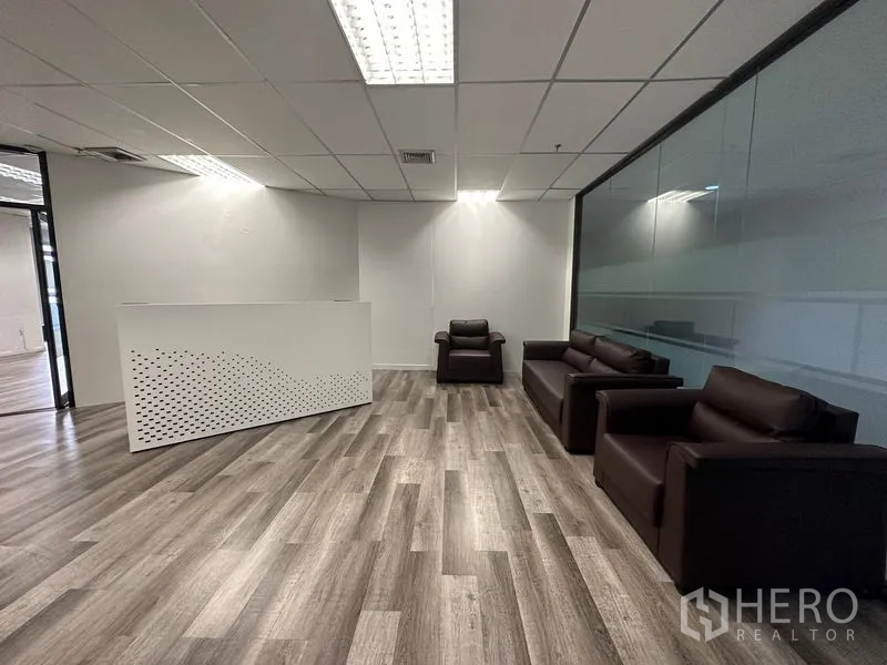 办公空间 出租或出售在Din Daeng, Bangkok - 接待区设白色前台与深色沙发，旁侧为整面玻璃墙。