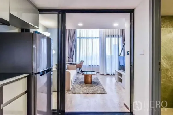 Condominium for rent in Huai Khwang, Bangkok - Sliding glass door from kitchen opens to bright living room with sofa and TV.
