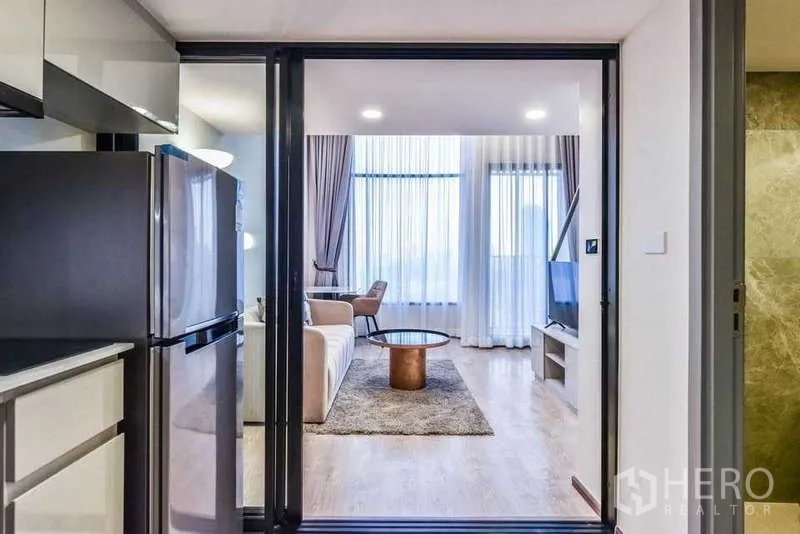 Condominium for rent in Huai Khwang, Bangkok - Sliding glass door from kitchen opens to bright living room with sofa and TV.