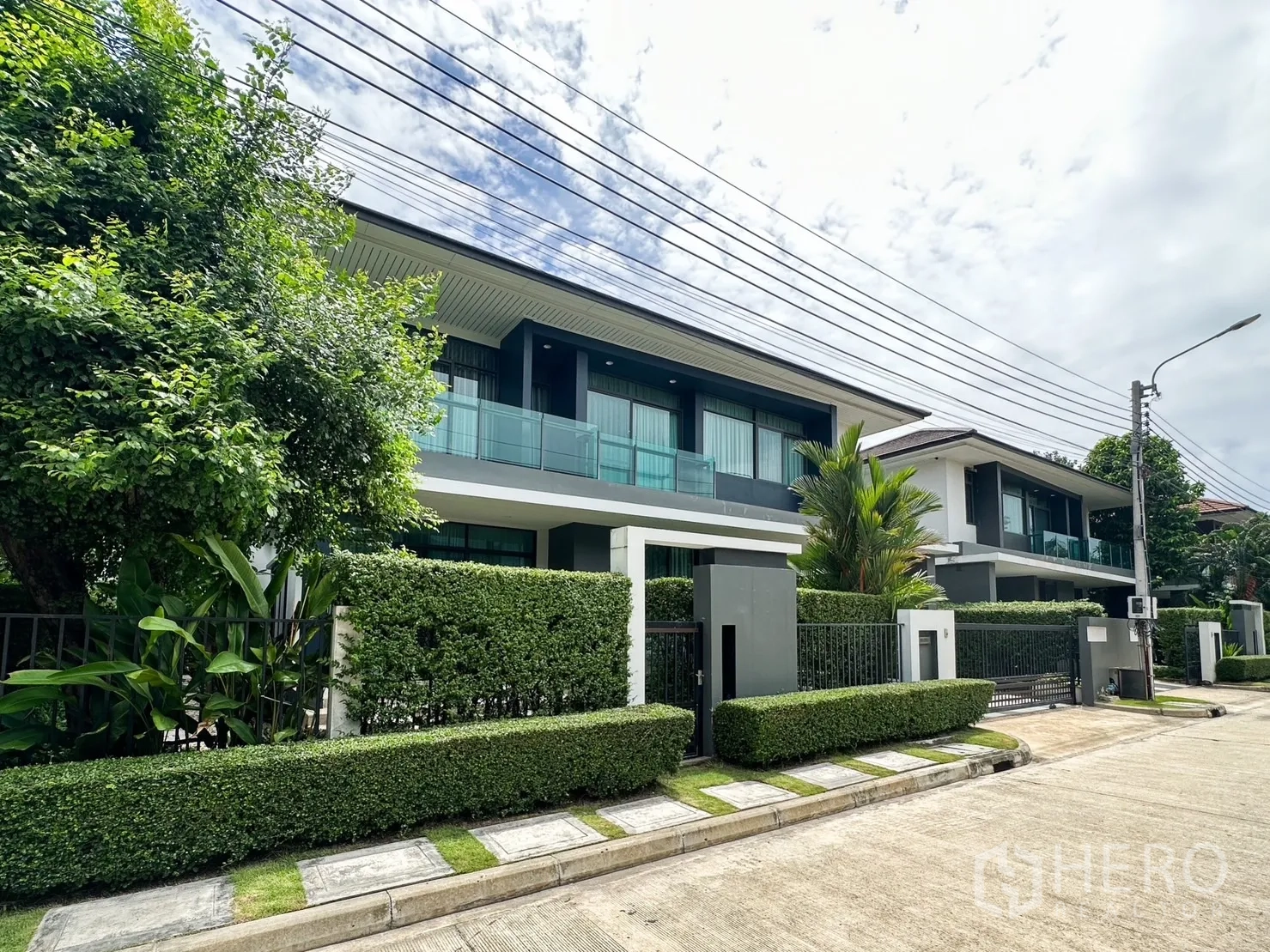 Detached House for rent or sale in Bang Kapi, Bangkok - Street view of an upscale residential row with landscaped hedges and contemporary glass-fronted balconies.