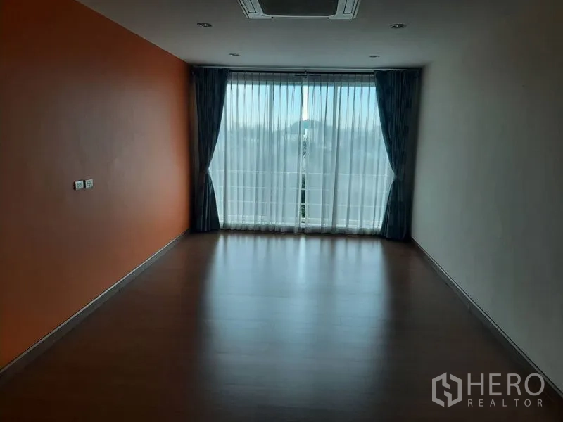 Home Office for sale in Phra Khanong, Bangkok - Empty room with an orange accent wall, full-height curtains and balcony light.