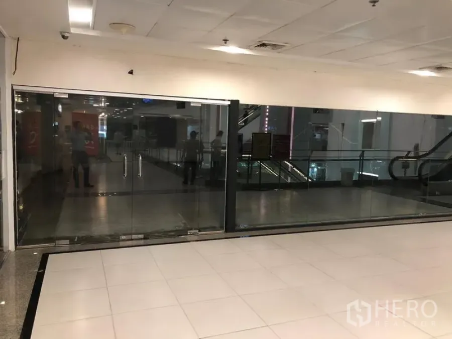 零售空间 出租在Watthana, Bangkok - 购物中心走道旁的空置玻璃门商铺，地砖地面，旁有自动扶梯