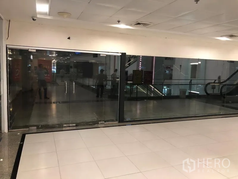 零售空间 出租在Watthana, Bangkok - 购物中心走道旁的空置玻璃门商铺，地砖地面，旁有自动扶梯