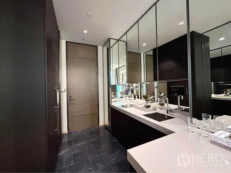 Condominium for rent in Pathum Wan, Bangkok - Modern galley kitchen with white quartz countertop, mirrored cabinets and an undermount sink.