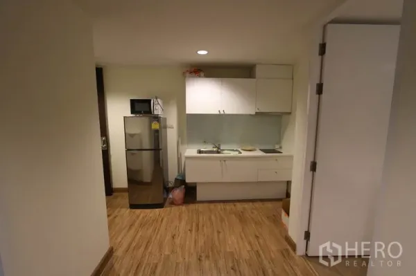 Condominium for rent or sale in Wang Thonglang, Bangkok - Compact kitchenette with white cabinets, sink, cooktop, microwave, and a stainless-steel refrigerator.