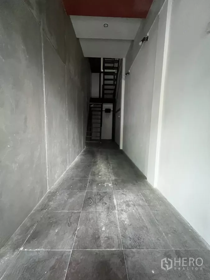 店屋 出租在Watthana, Bangkok - 狭长走廊铺砖，尽头连接黑色金属楼梯。