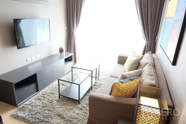Condominium for rent in Watthana, Bangkok - Bright living room with sofa, wall-mounted TV, long media console, and glass coffee tables by full-height curtains.