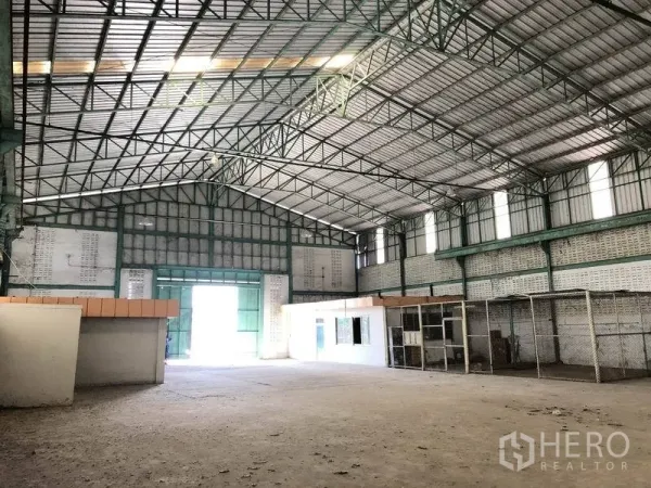 Warehouse for rent in Samut Prakan - High-bay warehouse area with wide entry door, office block, and caged storage section.