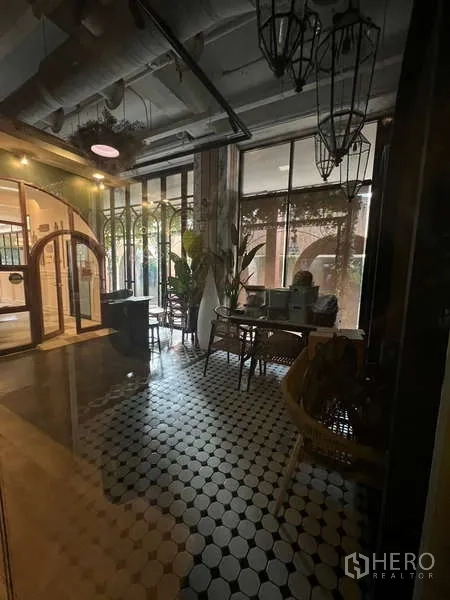 零售空间 出租在Watthana, Bangkok - 带黑白花砖地面、落地窗、吊灯与绿植的休憩区。