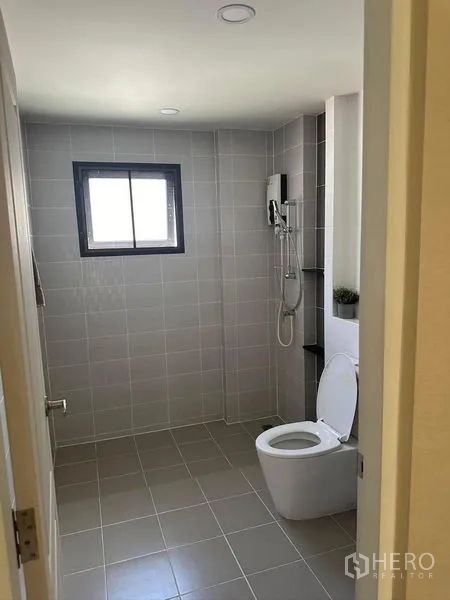 Detached House for rent in Bang Phli, Samut Prakan - Gray-tiled bathroom with window, toilet and walk-in shower with water heater.