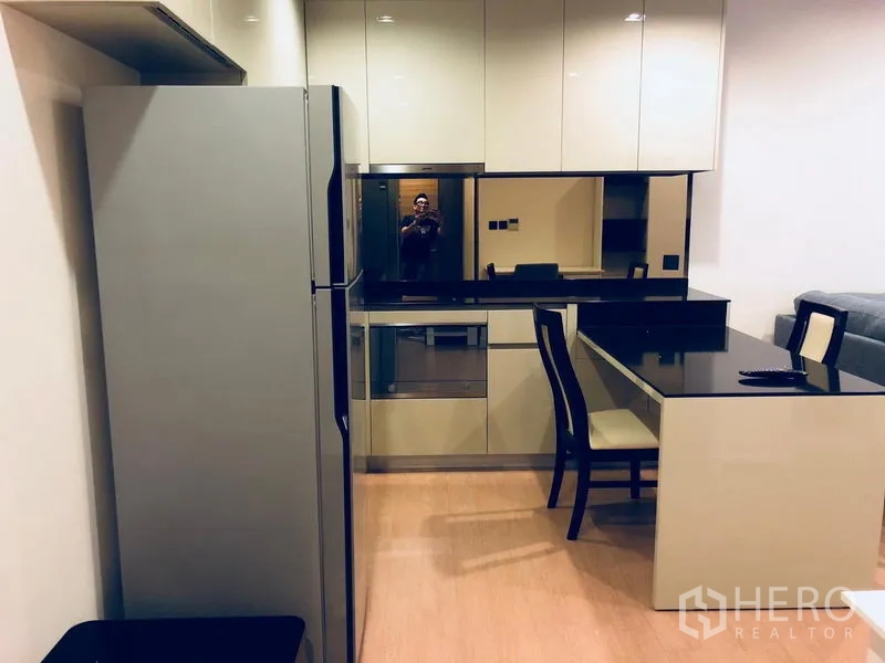 公寓 出租或出售在Bang Rak, Bangkok - 现代厨房，亮面橱柜、黑色台面、嵌入式烤箱和大冰箱。