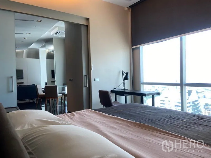 公寓 出租在Sathon, Bangkok - 从卧室望向起居区，落地窗旁配置书桌，可观城市景色。