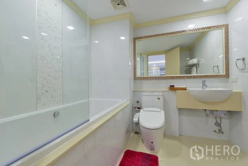 房间 出租在Khlong Toei, Bangkok - 现代白色浴室，大镜面、带玻璃挡板的浴缸与坐便器。