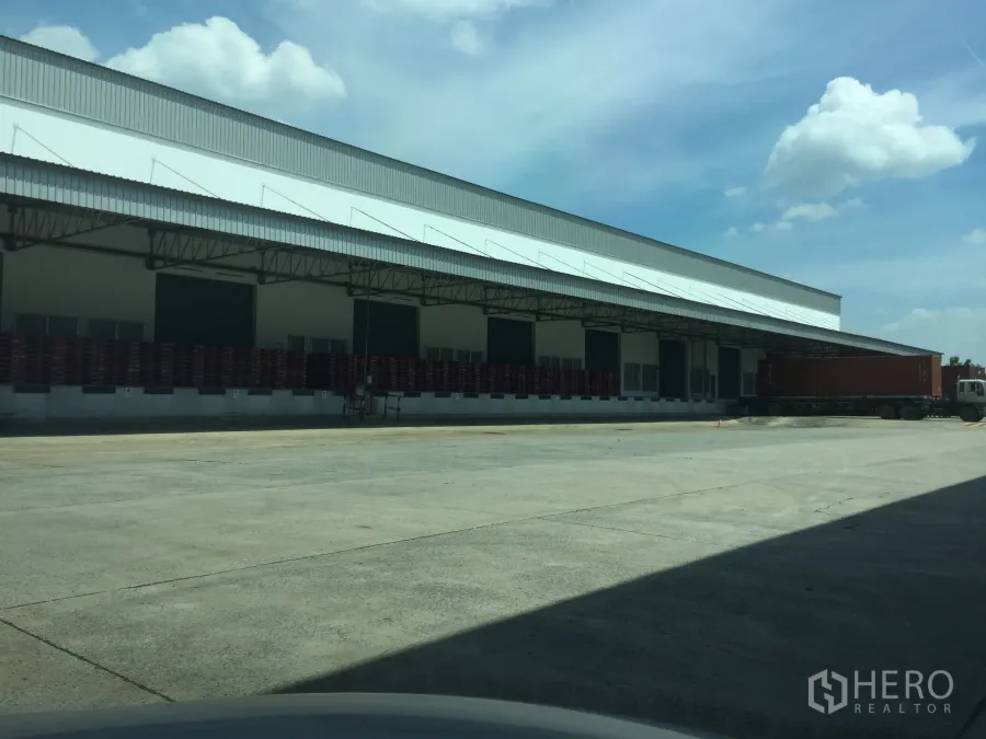 货栈 出租在Khlong Luang, Pathum Thani - Khlong Luang仓库外观，带大雨棚的装卸月台与多处卸货门，集装箱卡车停靠。