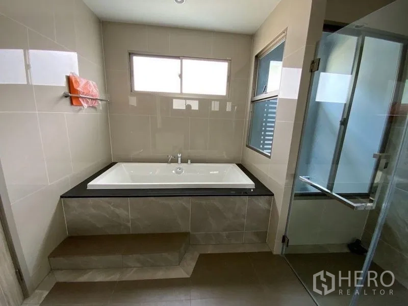 联排别墅 出租在Prawet, Bangkok - 浴室设抬高浴缸、玻璃淋浴间与窗户。