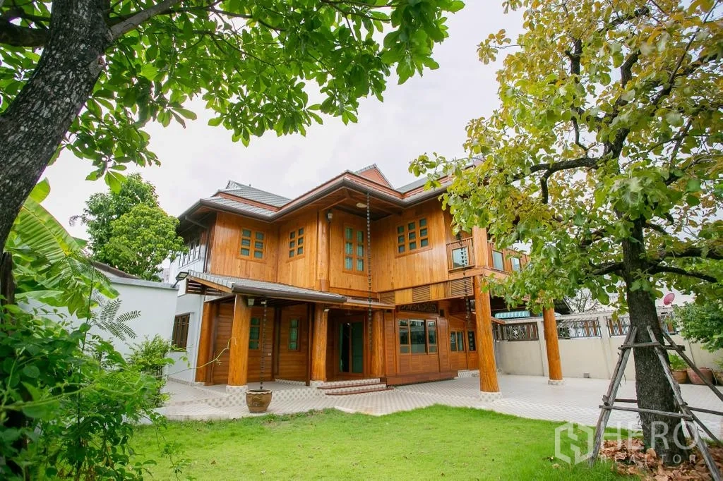 Detached House for rent or sale in Huai Khwang, Bangkok - Front garden view of a two‑storey timber house with lawn and trees.