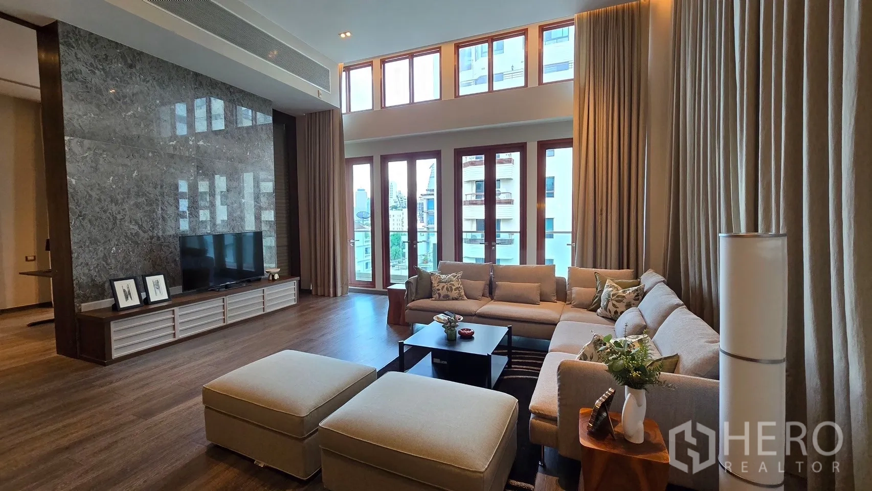 Condominium for rent - Double-height living room with floor-to-ceiling windows, city view, sectional sofa and TV wall.
