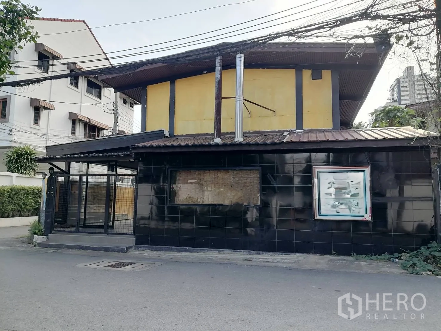 Detached House for rent in Watthana, Bangkok - Street view of the house with a black tiled facade, sliding gate, and pitched roof.