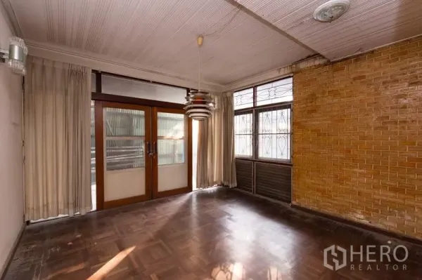 บ้าน ให้เช่าในKhlong Toei, Bangkok - ห้องนั่งเล่นสไตล์วินเทจ พื้นปาร์เกต์ ผนังอิฐตกแต่ง หน้าต่างผ้าม่าน และประตูกระจกบานคู่ ในบ้านเดี่ยวโซนทองหล่อ