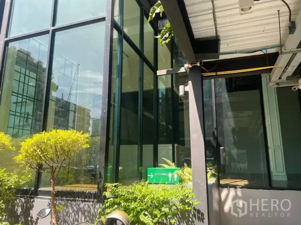 零售空间 出租在Khlong Toei, Bangkok - 现代玻璃建筑转角外立面，绿化与有顶走道，曼谷城市环境